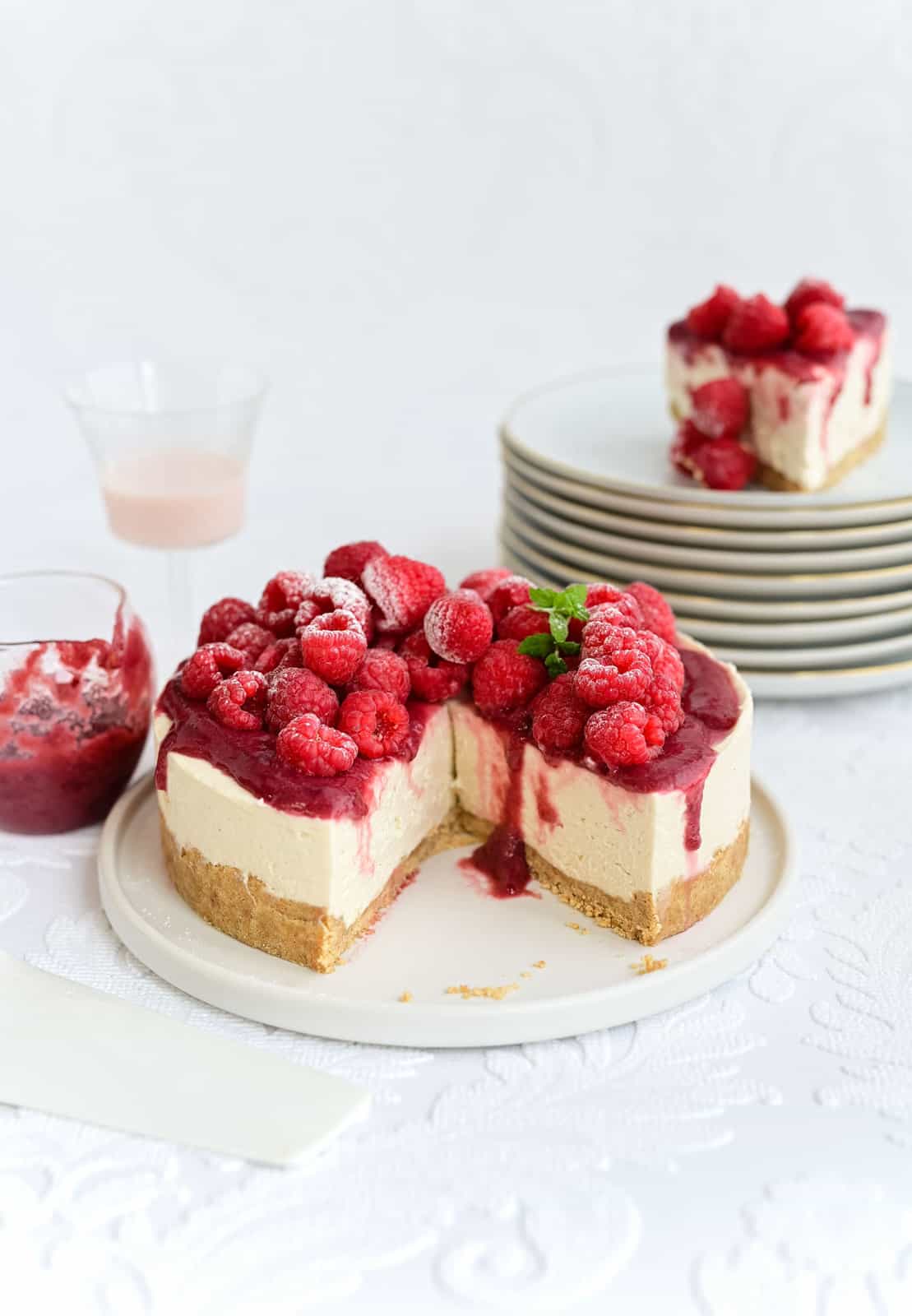 White Chocolate Raspberry Cheesecake topped with fresh raspberries on a white plate with a large slice cut out