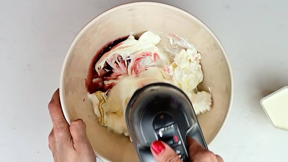 Beating mascarpone, jam, vanilla and cream using a hand mixer