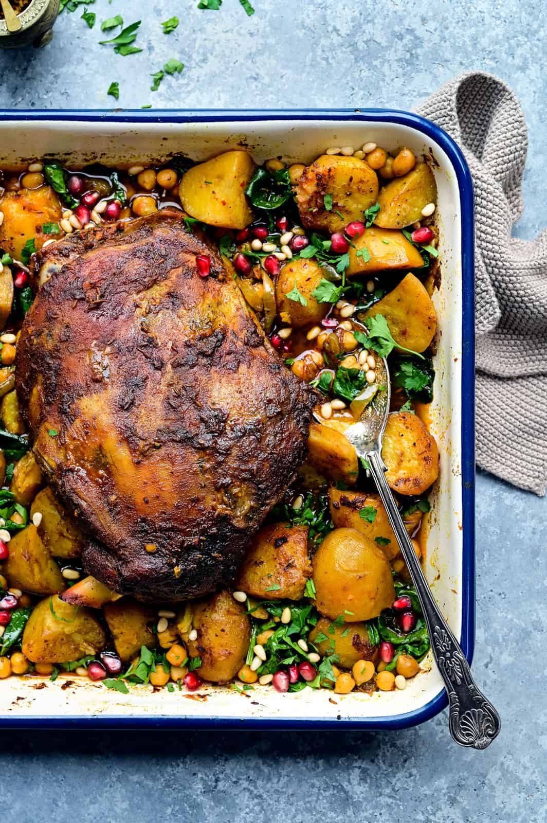 Overhead view of a roasting tin with roast potatoes, chickpeas, spinach and slow cooked lamb shoulder