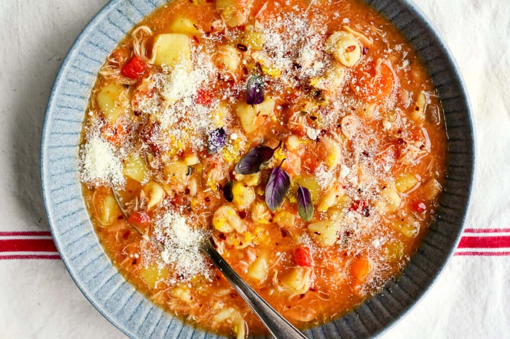bowl of hearty chicken soup with pasta, tomatoes, peppers and soffrito