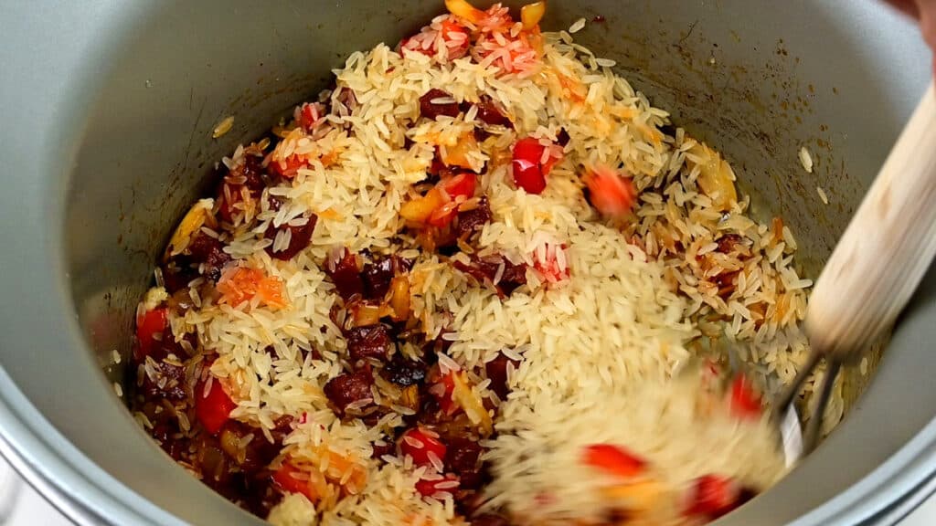 Stirring rice into cooked chorizo, onions and red pepper cooking in a slow cooker