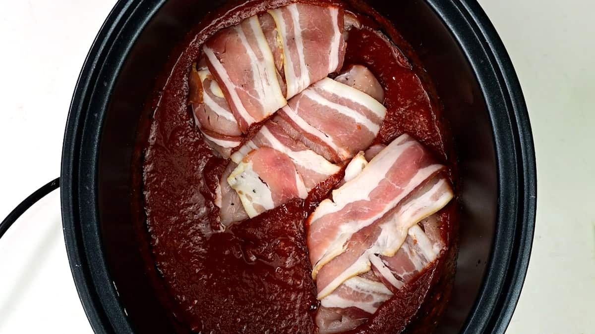 Bacon wrapped chicken breasts in BBQ sauce in a crockpot