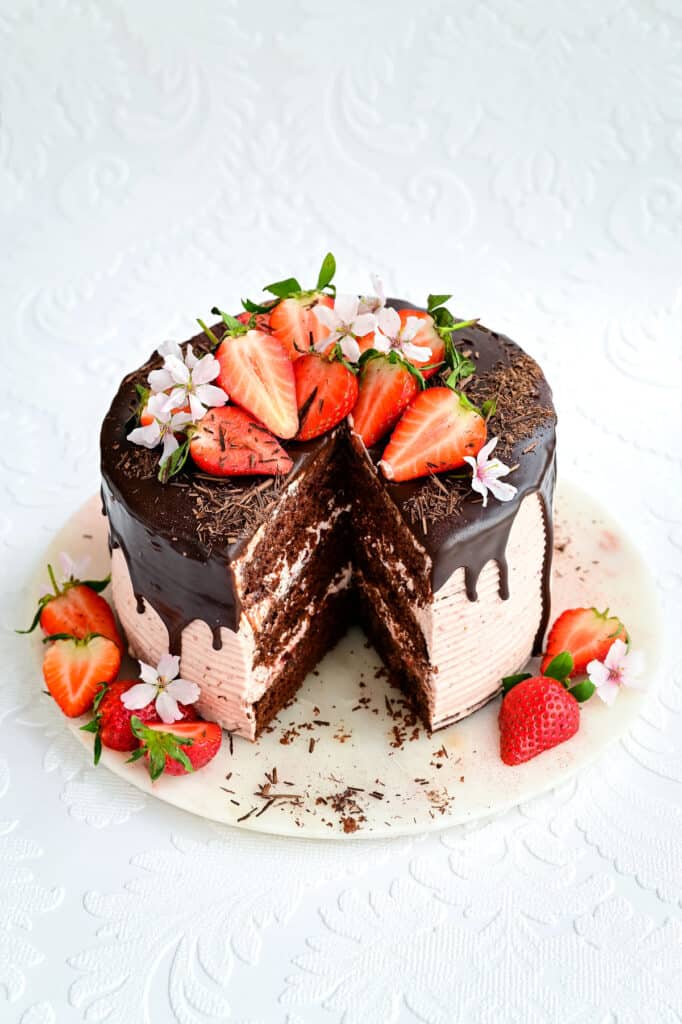 Chocolate strawberry layer cake on a marble platter with slice cut out