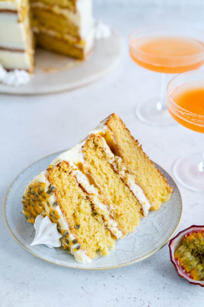 Slice of passion fruit layer cake on a plate with cocktails in the backgrounds