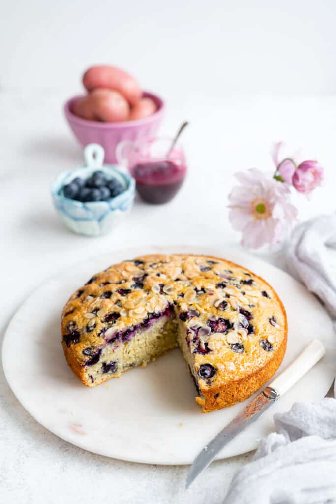 Blueberry almond cake on a marble plate with large slice cut out