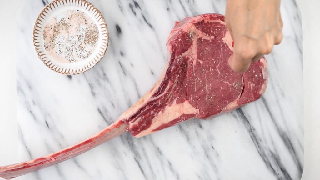 seasoning a large steak with salt and pepper