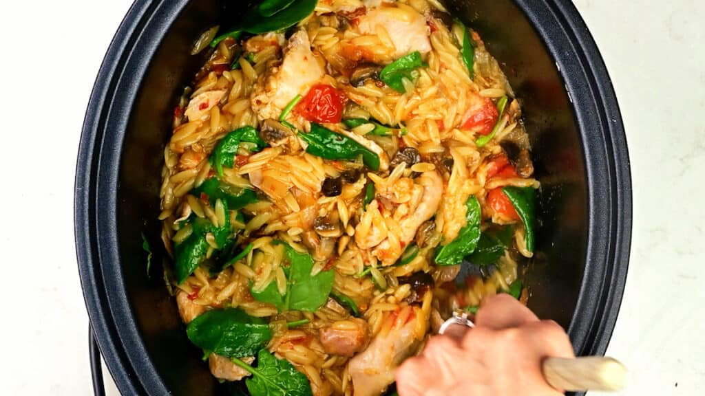 Stirring fresh spinach into slow cooker chicken pasta 