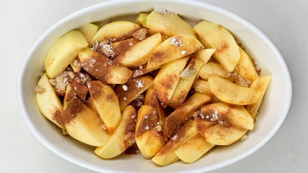Apples tossed with sugar and cinnamon in a baking dish