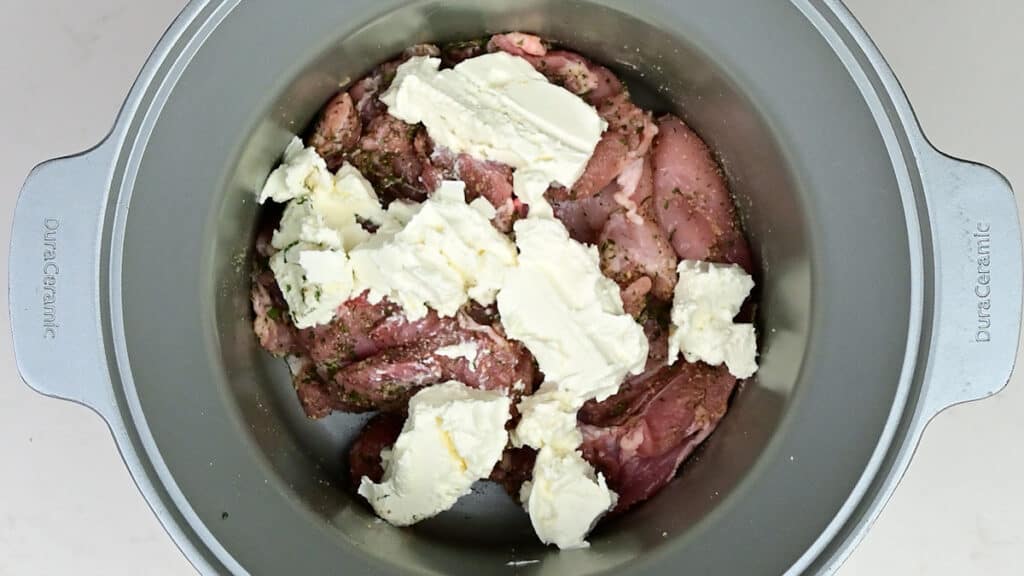 chicken thighs topped with cream cheese in a slow cooker