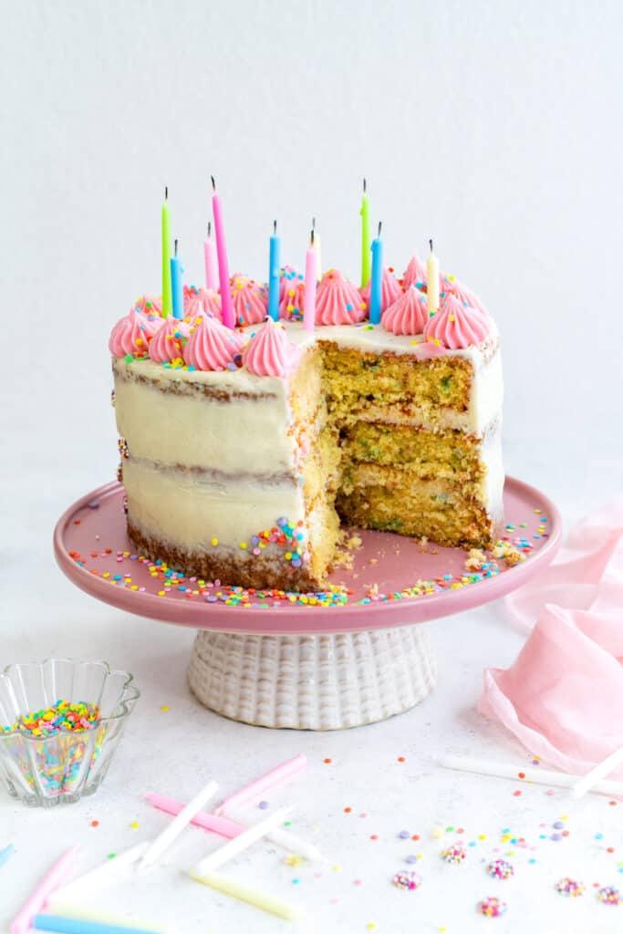 Sliced Funfetti Layer cake on a cake stand decorated with sprinkles and birthday candles