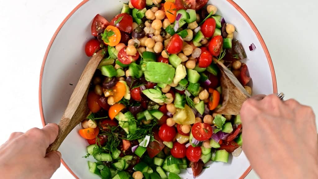 Tossing vegan chickpea salad in a bowl