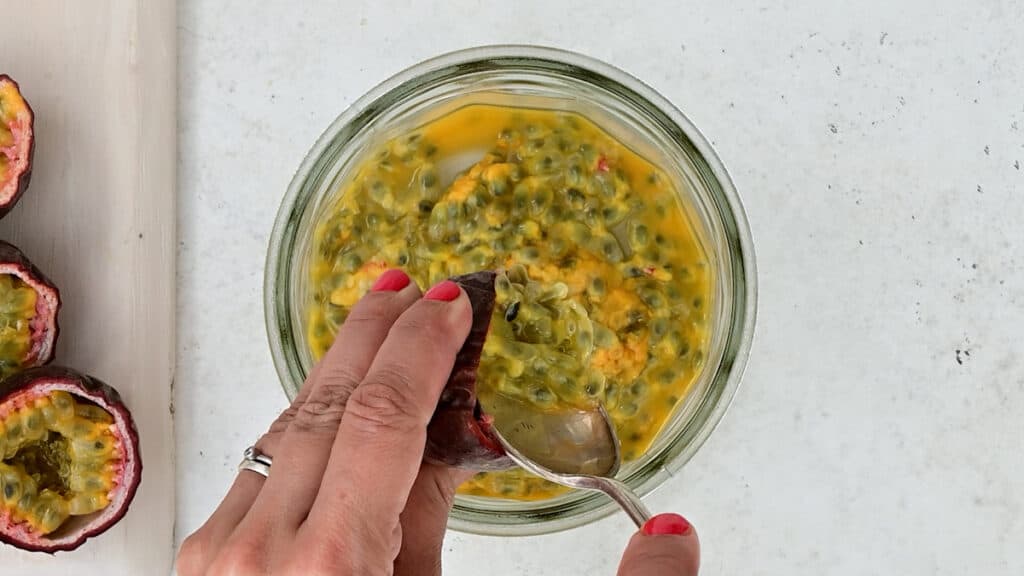 scooping out passion fruit pulp into a jar