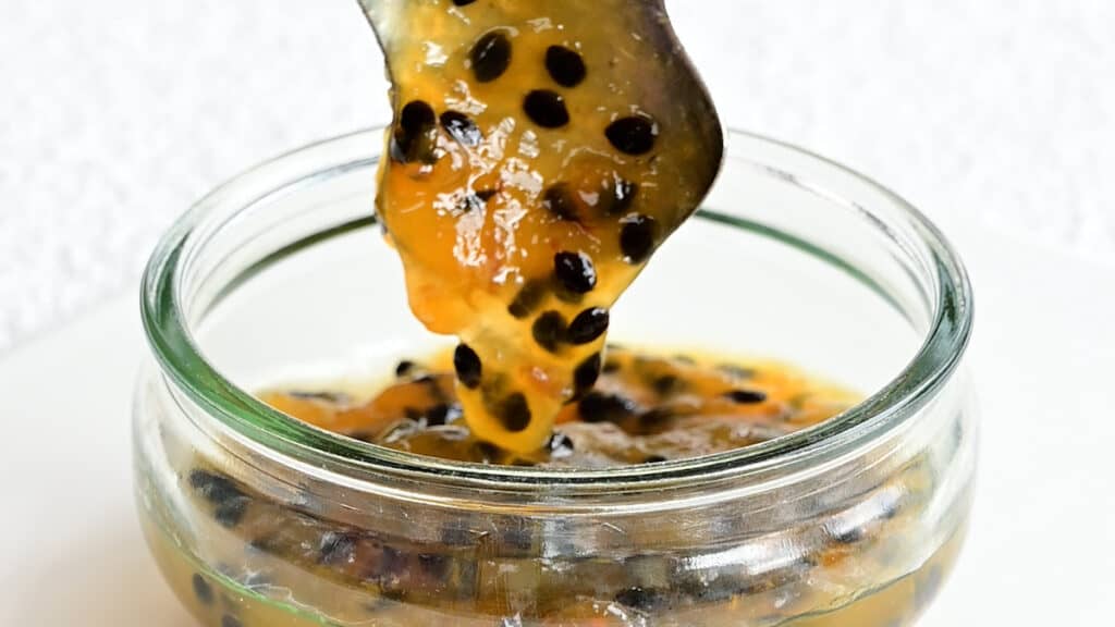 spooning passion fruit jam into a small jar