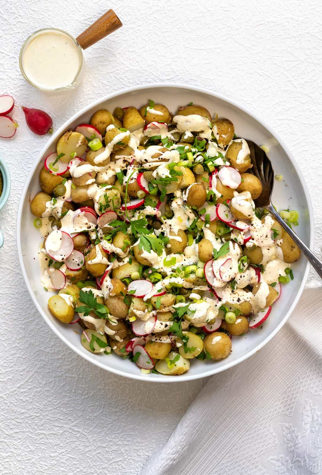 New potato salad with Jersey Royals, radish, spring onions, pickles and a healthy creamy dressing in a bowl