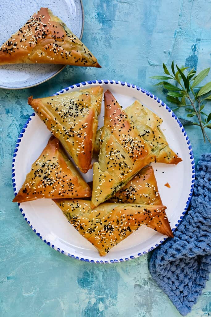 Spanakopita triangles topped with sesame seeds on a plate