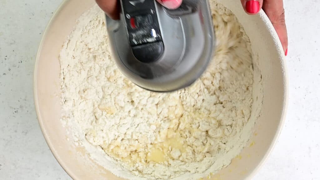 beating yogurt cake batter in a mixing bowl with an electric hand mixer