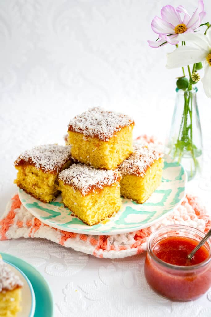 Squares of jam and coconut sponge piled on a plate