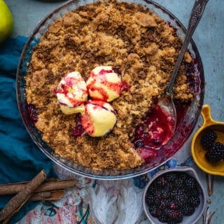 Apple and Blackberry crumble topped with ice cream in a glass pie dish