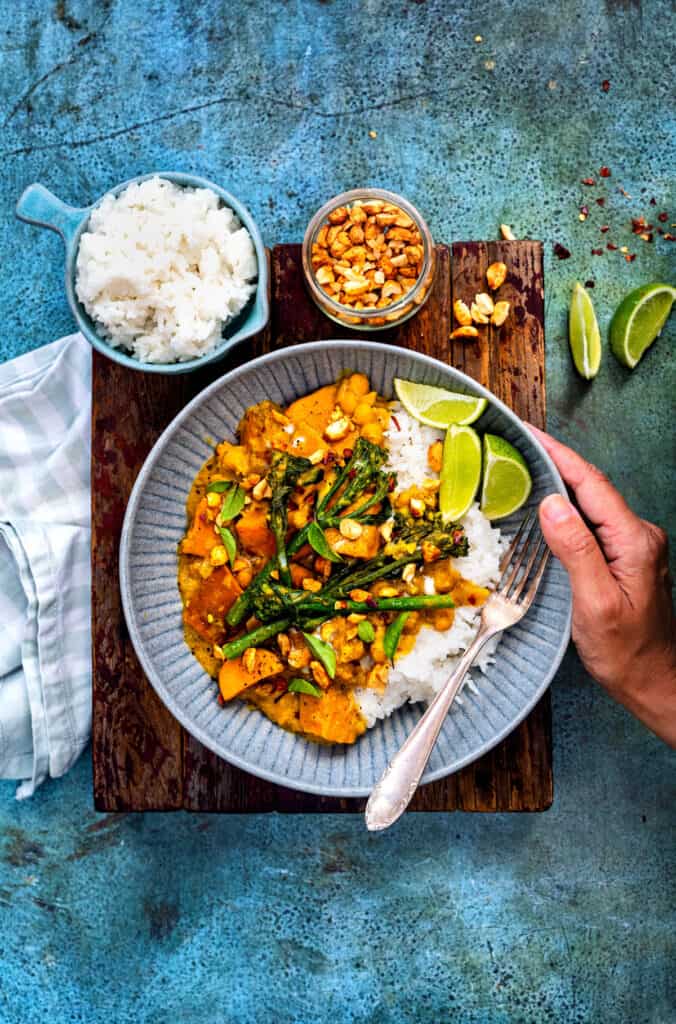 Satay sweet potato curry in a bowl served over jasmine rice with lime wedges on the side