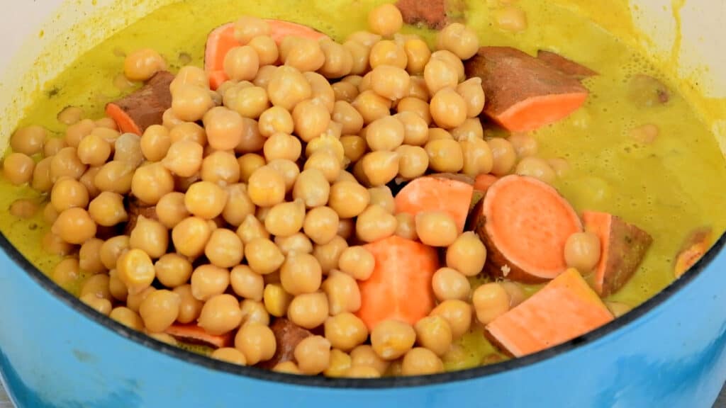 Chickpeas and sweet potatoes added to pot of vegan curry sauce