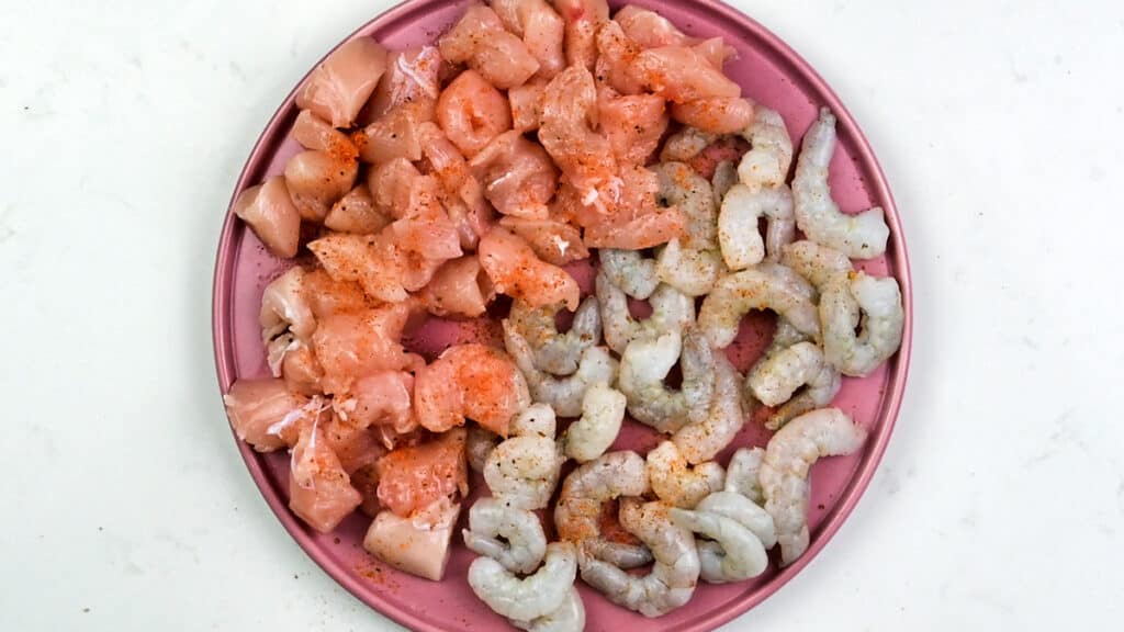 diced chicken breast and raw shrimp with Cajun seasoning on a pink plate
