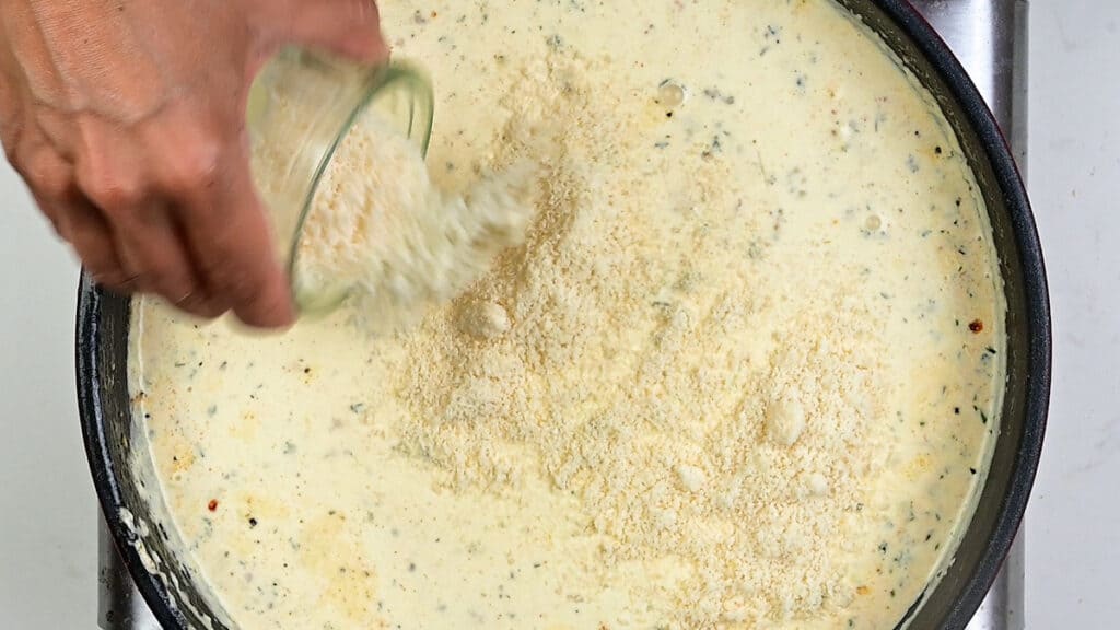adding grated Parmesan cheese to pan of Alfredo sauce