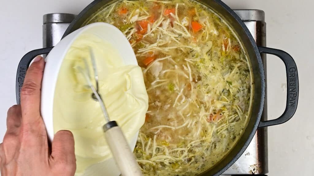 adding cream cheese to pot of chicken soup