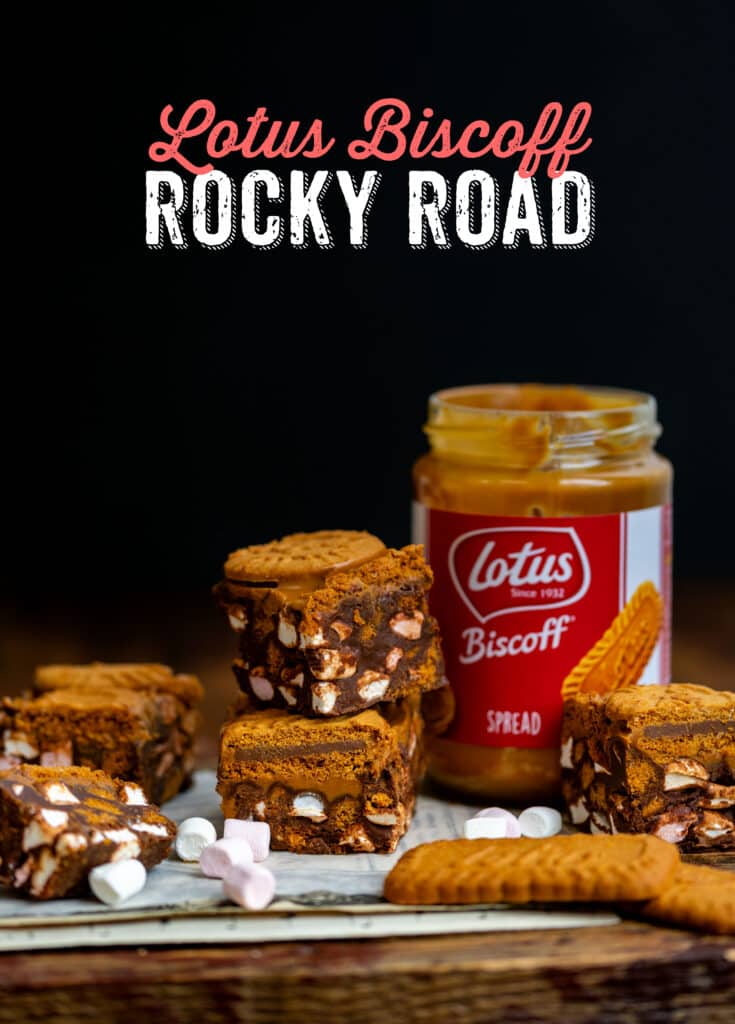 Biscoff rocky road squares stacked on a board with a jar of Lotus Biscoff spread on the side