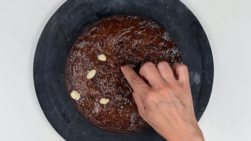 Brushing fruitcake with apricot jam and filling small holes with pieces of marzipan