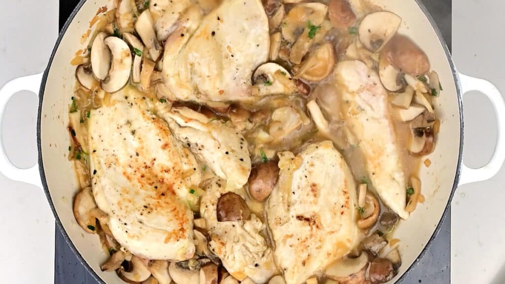 chicken cooking with mushrooms and stock in a pan