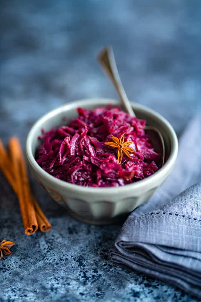 Braised red cabbage in a grey bowl with cinnamon sticks on the side