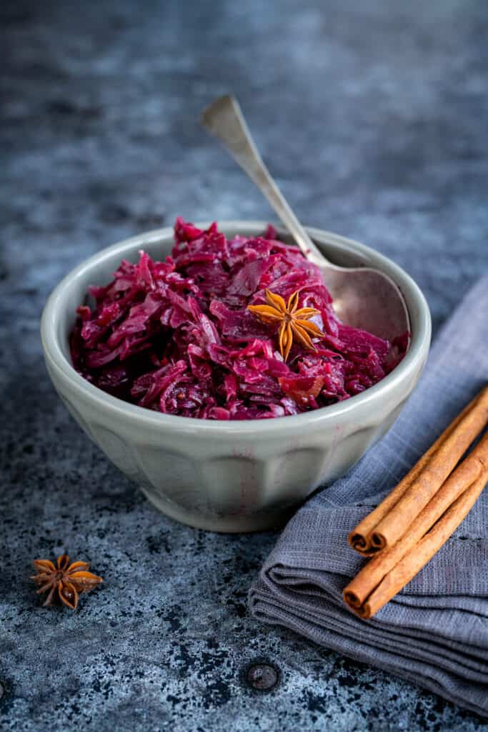 Braised red cabbage in a grey bowl with cinnamon sticks on the sdie