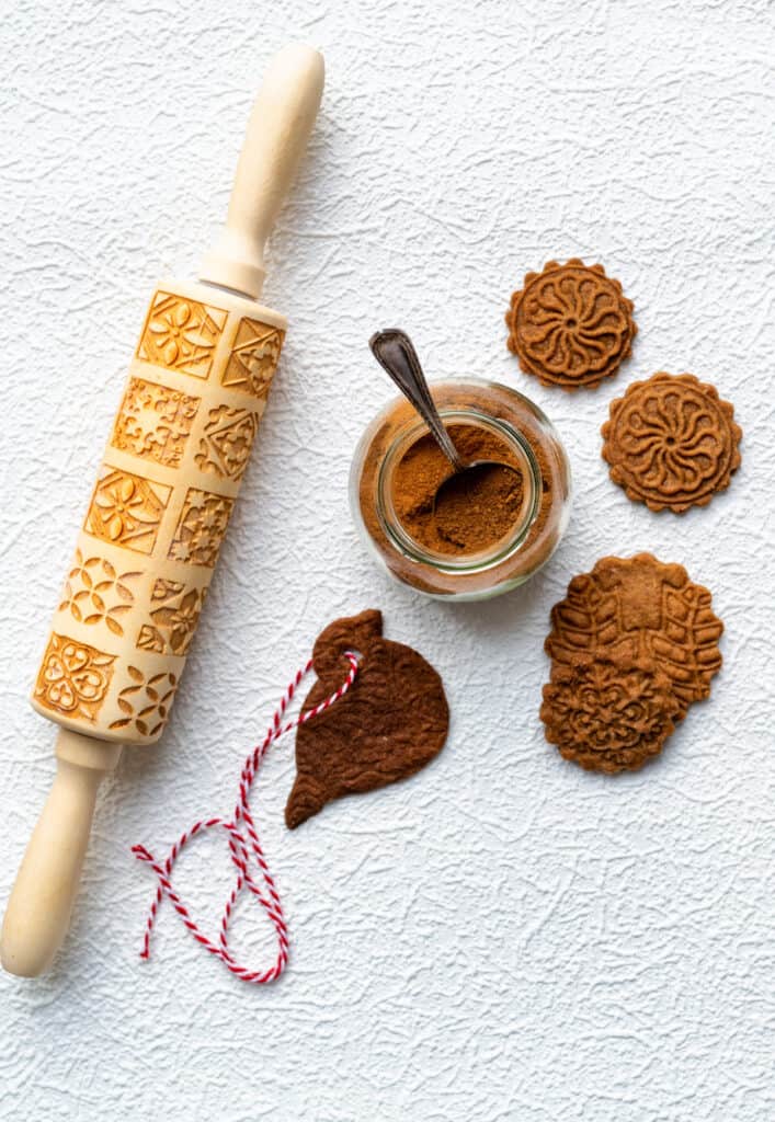 Speculoos spice mix in a jar surrounded by cookies and a rolling pin