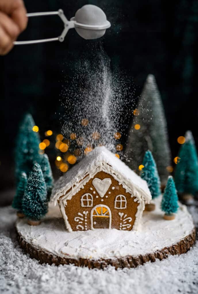 Dusting a small gingerbread house with powdered sugar