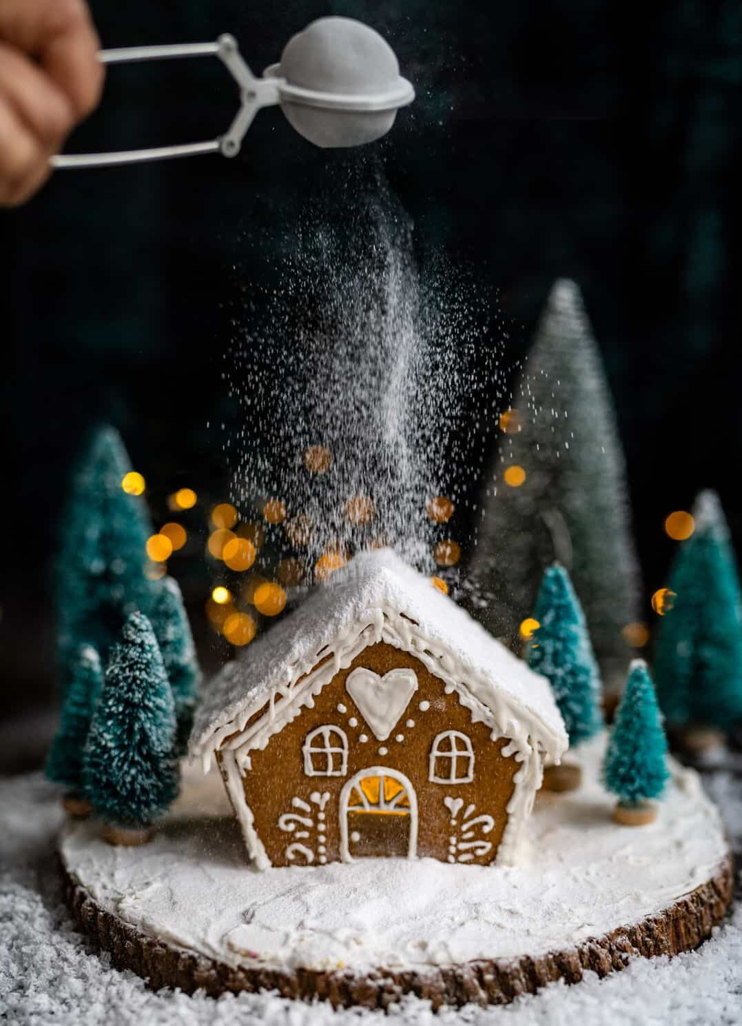 Dusting a small gingerbread house with powdered sugar