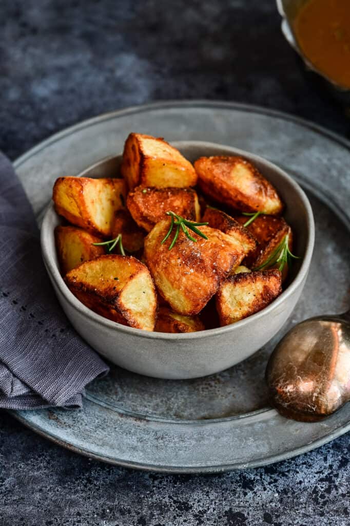 Bowl of crunchy roast potatoes garnished with rosemary