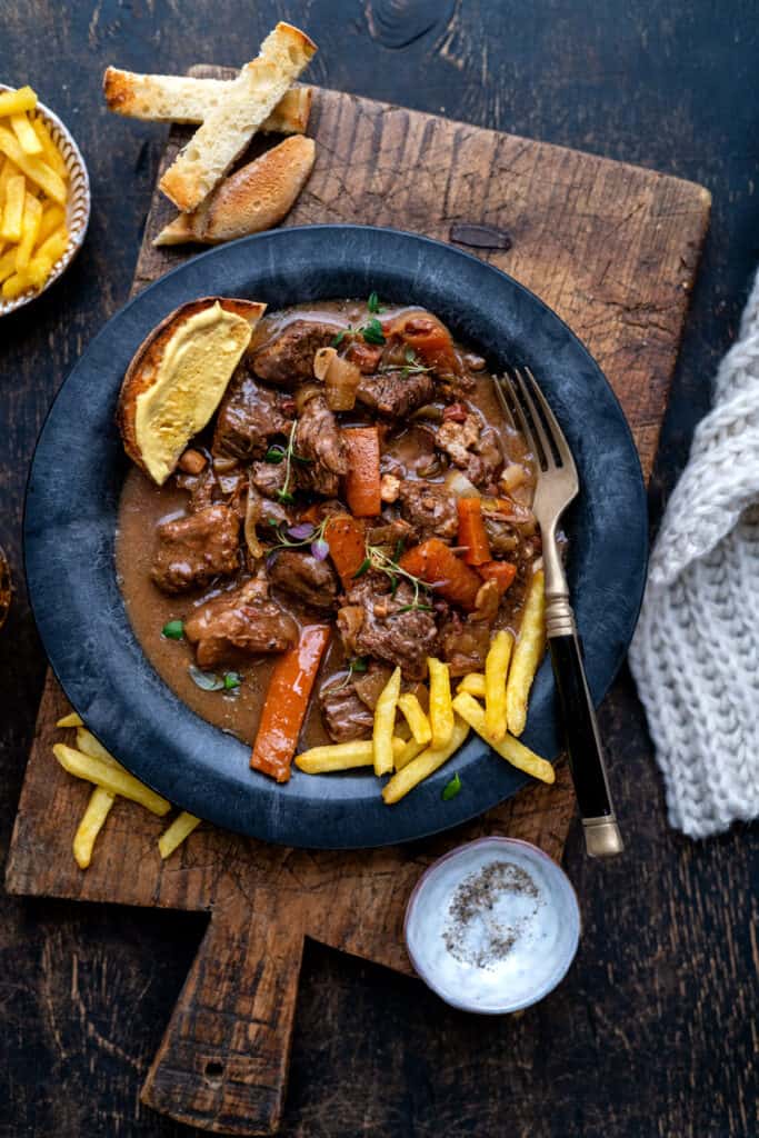 Bowl serving of Beef Carbonnade with fries and bread on the side