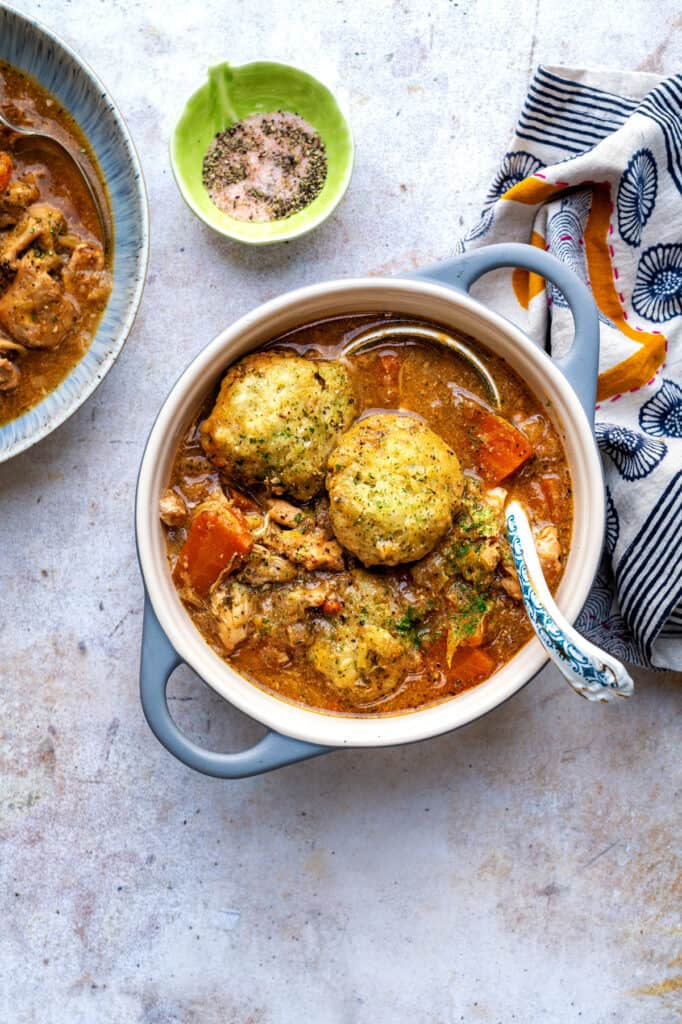 Overhead photo of chicken stew and dumplings in a ceramic pot