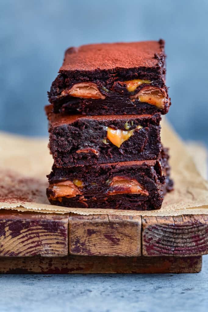 Stack of three salted caramel brownies on a wooden board