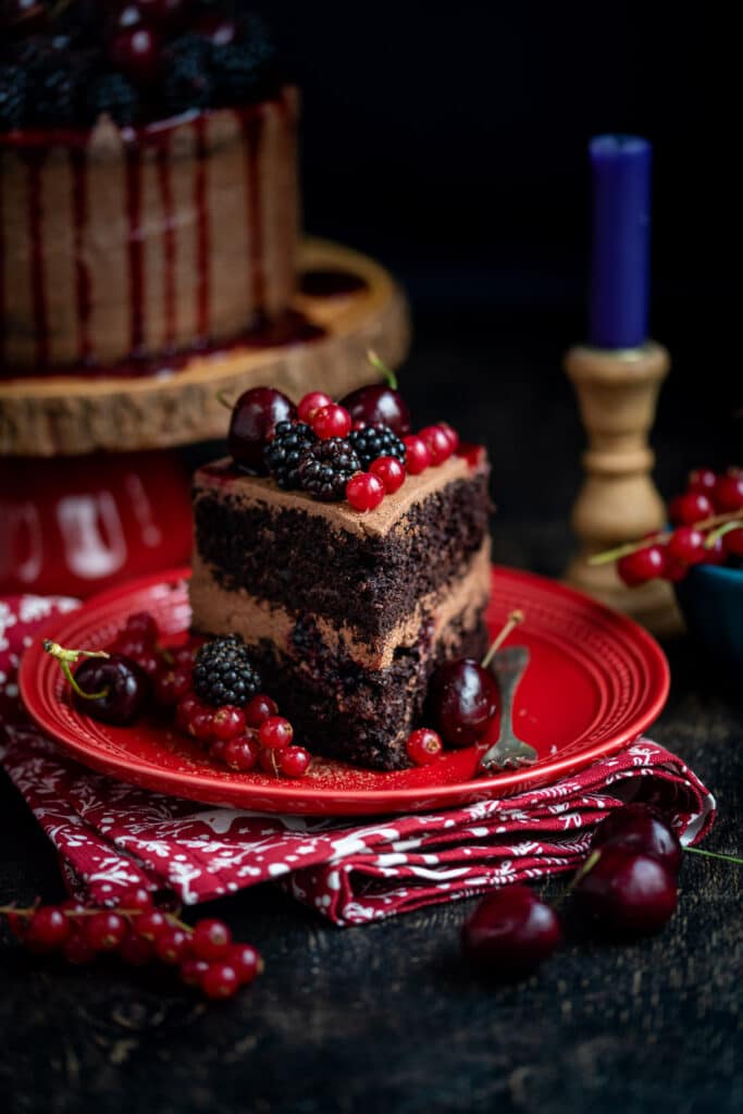 slice of vegan chocolate cake topped with berries on a red plate