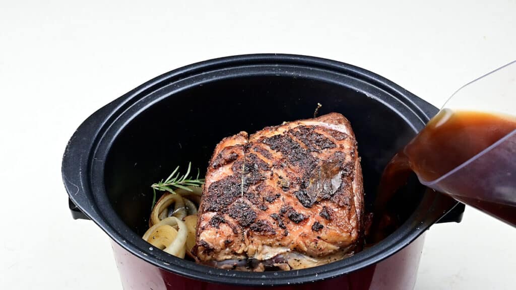 Rib of beef in a slow cooker with broth being added