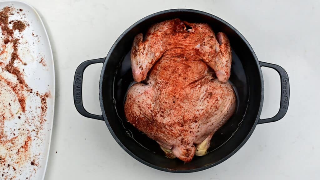Whole seasoned chicken placed in a Dutch oven breast side down