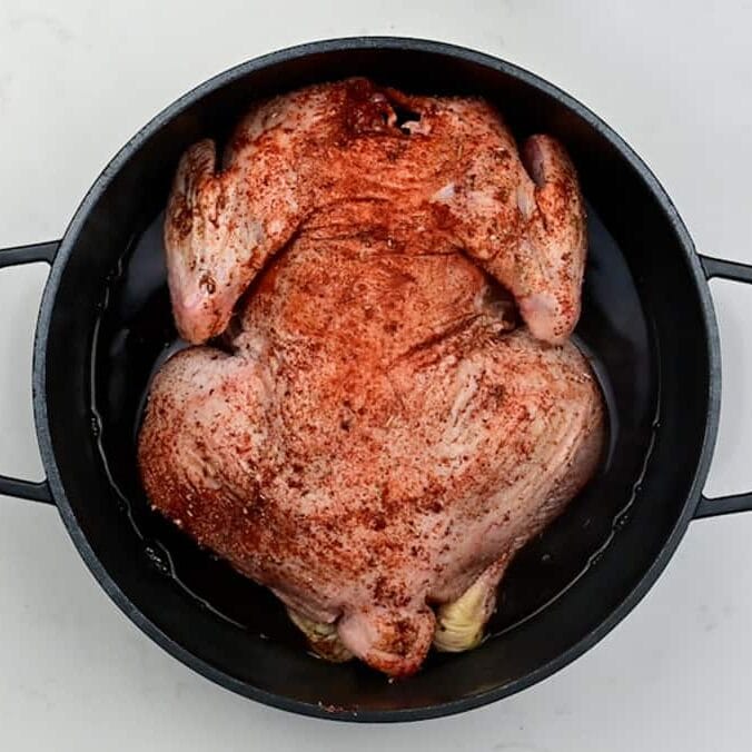 Whole seasoned chicken placed in a Dutch oven breast side down