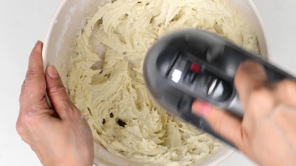 beating buttercream in a bowl using a hand mixer