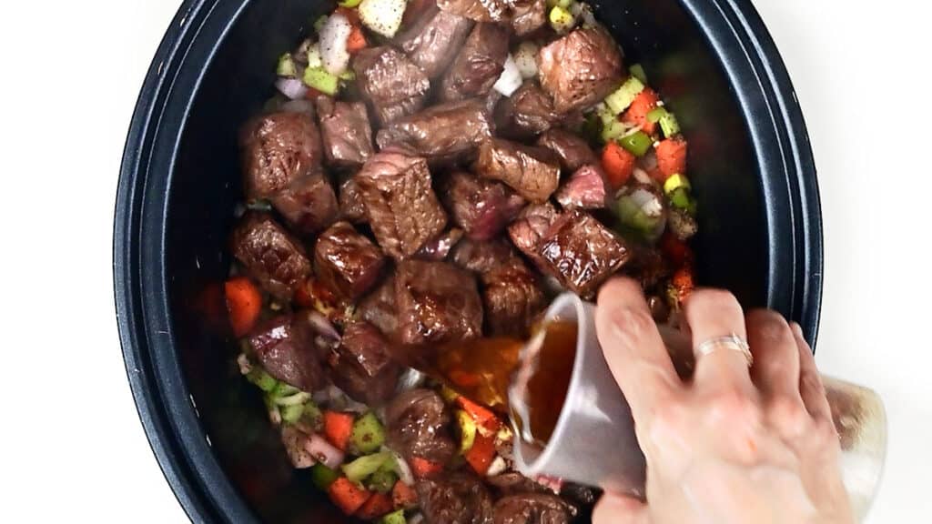 adding ale to a slow cooker with browned beef cubes and vegetables