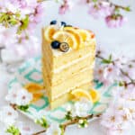 Slice of lemon cake decorated with lemon slices and blueberries among fresh flowers