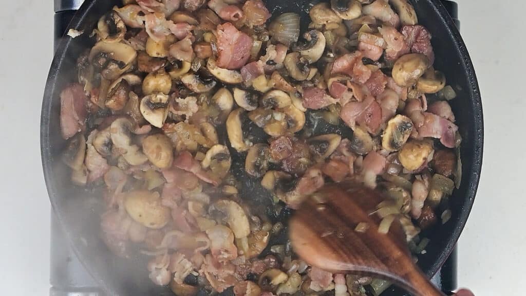 panfrying onions, bacon and mushrooms in a pan