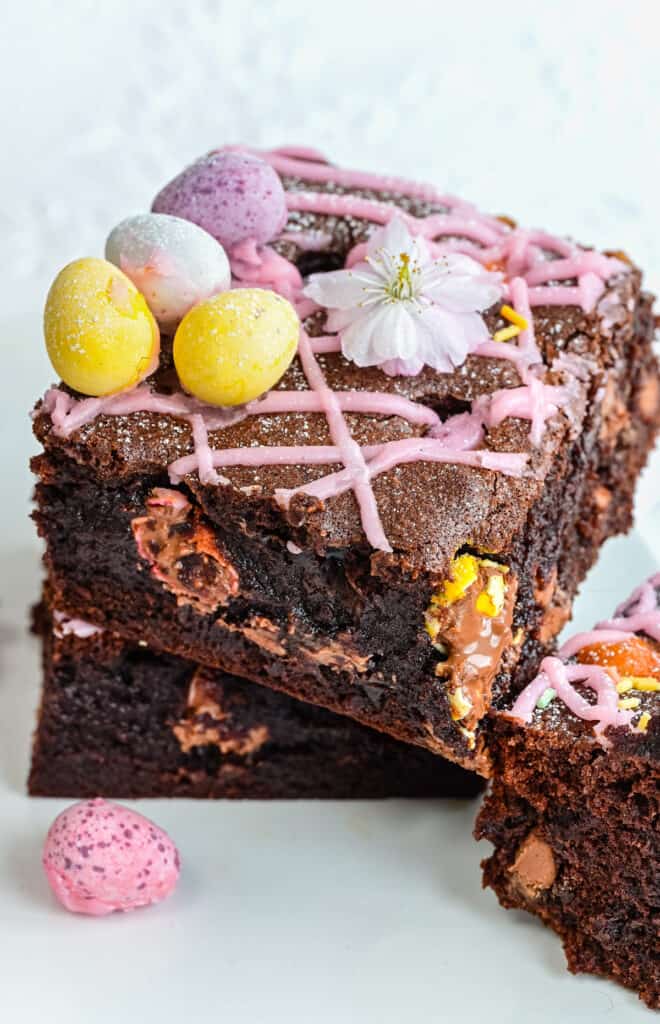 Close up on two squares of mini egg brownies topped with pink icing and Cadbury's Mini Eggs