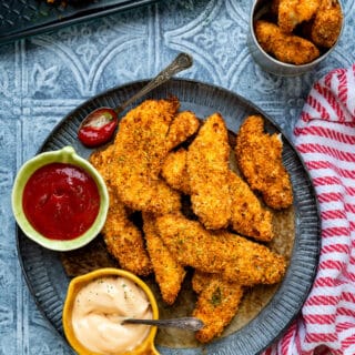 Plate with crispy chicken goujons and small bowls of ketchup and mayonnaise