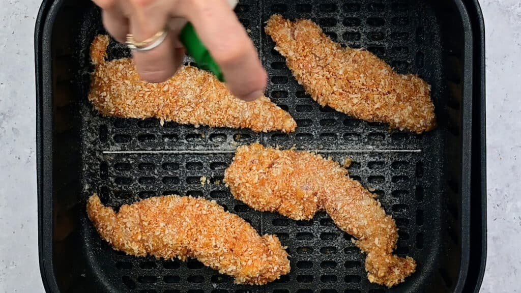 Misting chicken goujons with cooking spray in the basket of an air fryer